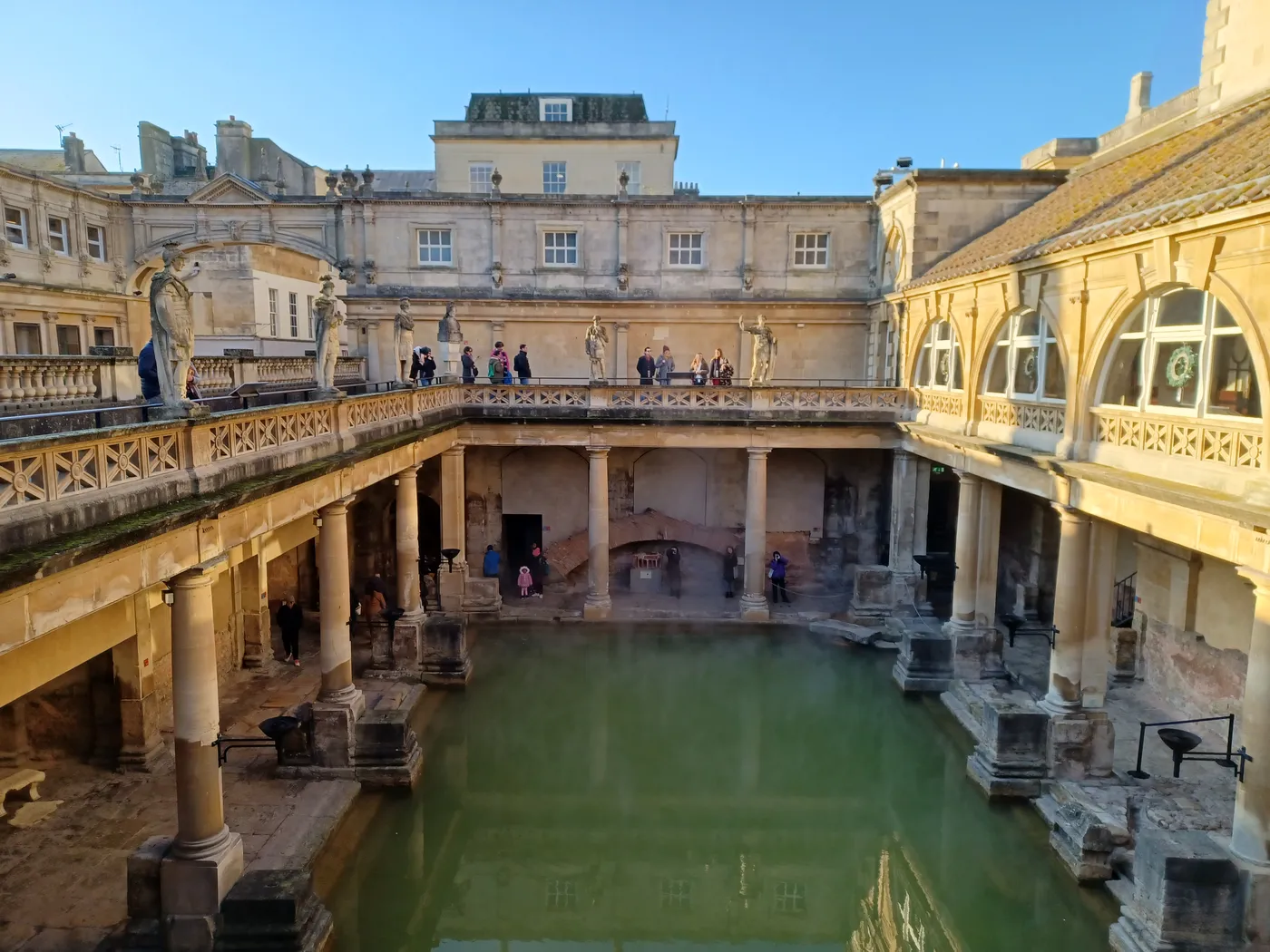 The Great Bath with green water, seen from the upper terrace of the Roman Baths with stone columns around it