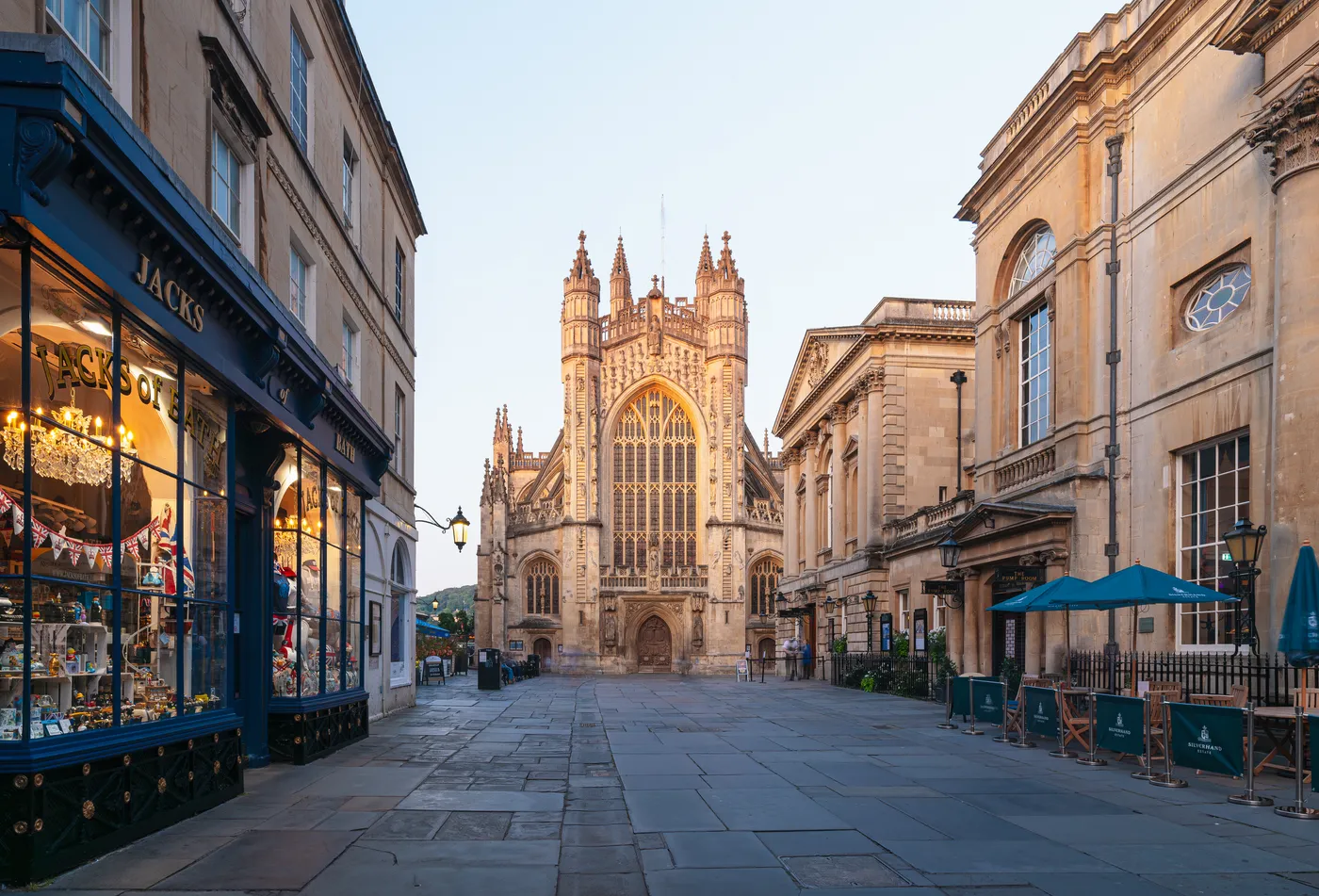 Bath Abbey seen along a paved street lined with Georgian buildings and shops